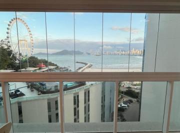 Vista da sacada: o mar, a roda-gigante e a orla de Balneário Camboriú, entre prédios vizinhos · Apartamento com vista mar à venda no Ed. Santé em Balneário Camboriú