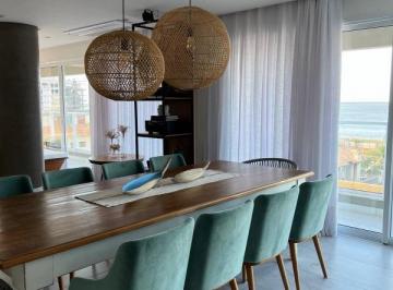 Sala de jantar com mesa longa de madeira e o mar visto pela janela · Apartamento 222 m² com 3 suítes e vista mar no Brava Arts, Itajaí